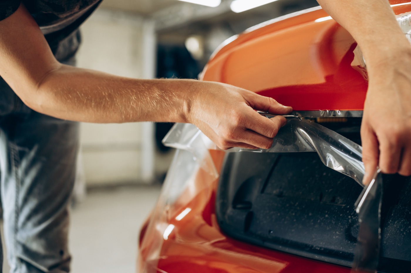 Installer fitting clear paint protection film to the rear bumper of an orange car